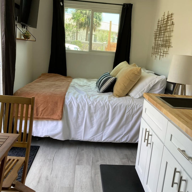 Small bedroom with bed, chair, and kitchen counter.